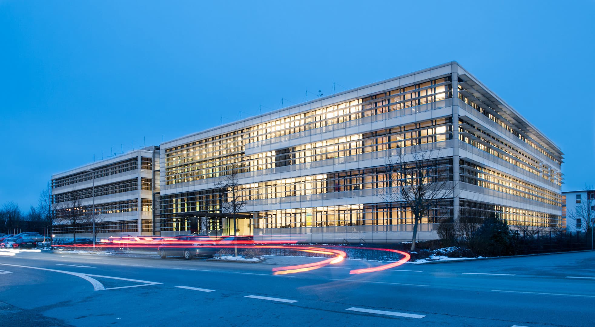 Modernes Bürogebäude der Baaderbank in Unterschleißheim mit beleuchteten Fenstern am Abend.