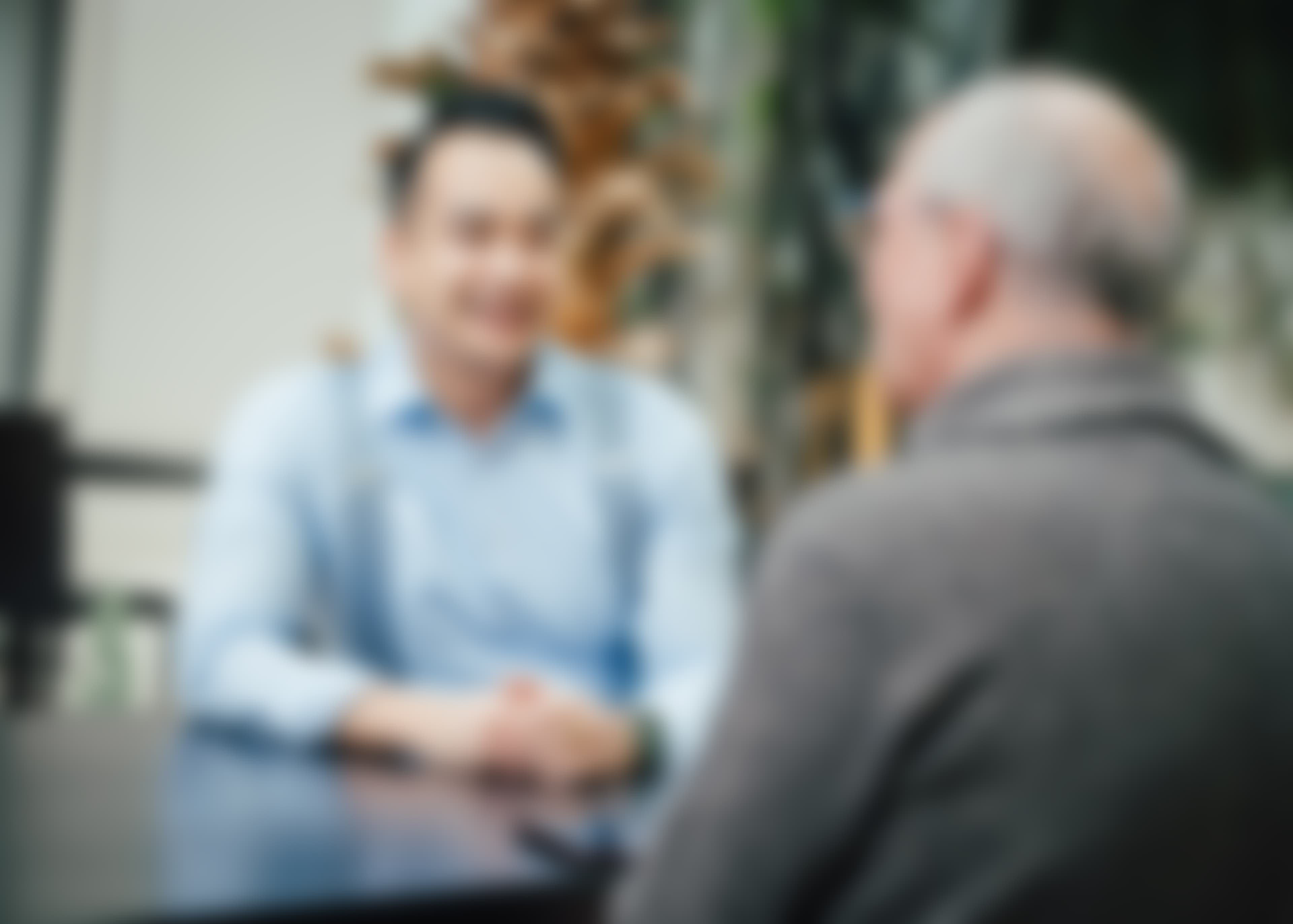 Verschwommene Aufnahme von zwei Personen im Gespräch in einer modernen Umgebung.